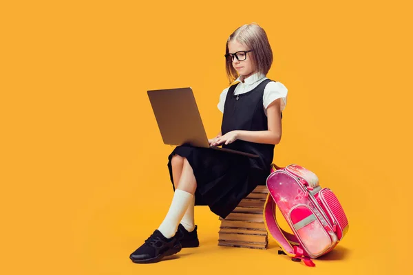 Full length μαθήτρια με στολή κάθονται στη στοίβα των βιβλίων εργασίας σε φορητό υπολογιστή. Έννοια εκπαίδευσης παιδιών. — Φωτογραφία Αρχείου
