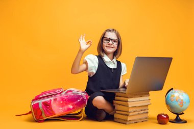  Gülümseyen öğrenci dizüstü bilgisayarlı kitapların arkasında oturur. Çocuk eğitimi.