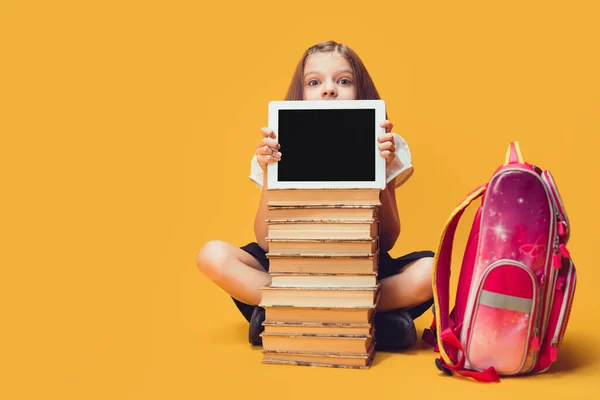 Schulmädchen blickt hinter einem Stapel Bücher hervor, Tablet schaut in die Kamera — Stockfoto