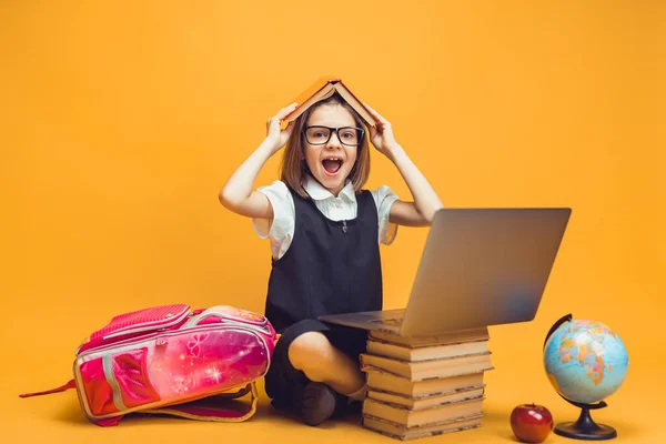 Emotionaler Schüler sitzt hinter einem Stapel Bücher, Laptop hält Buch auf dem Kopf. Bildungskonzept für Kinder — Stockfoto