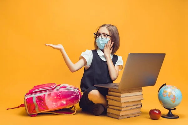 Elever i medicinsk mask sitter bakom en bunt böcker och laptop pekar tomrummet Kids utbildning — Stockfoto