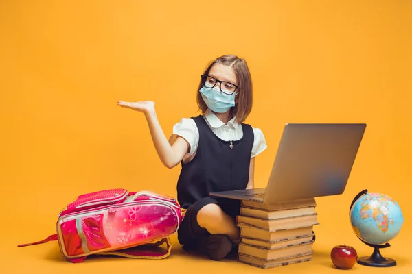 Elever i medicinsk mask sitter bakom en bunt böcker och laptop pekar tomrummet Kids utbildning — Stockfoto