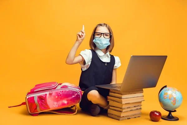 Elever i medicinsk mask sitter bakom en bunt böcker och laptop höjer pekfingret upp Kids utbildning — Stockfoto