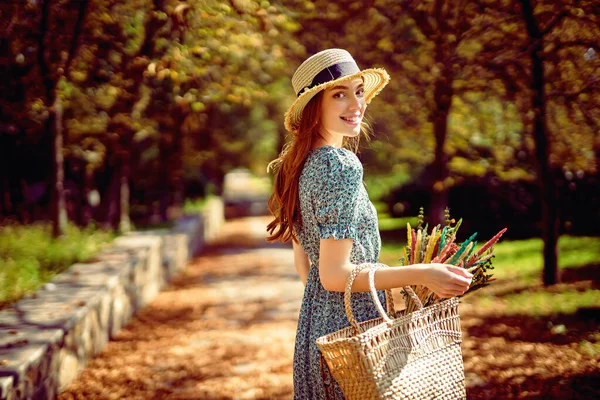 阳光灿烂、温暖的日子里，红头发的女孩一个人在秋天的公园里散步，同时还提着手提包- -印度夏天 — 图库照片