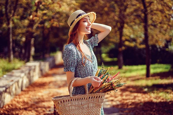 Felice rossa ragazza cammina da sola nel parco autunnale nella soleggiata giornata calda mentre tiene borsa estate indiana — Foto Stock