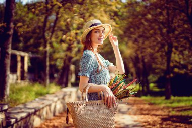 Gülen kızıl saçlı mutlu kız sonbahar parkında saman şapkasıyla yürüyor. Hint Yazı