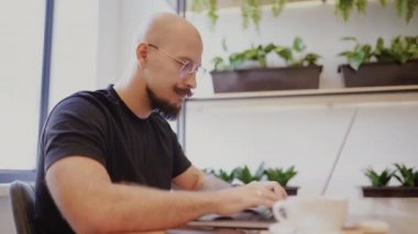 Bıyıklı, sakallı, gözlüklü, kafeteryadaki laptopta özenle çalışan beyaz bir iş adamı..