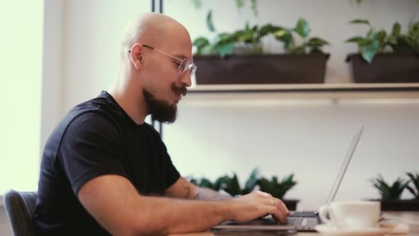 Schöner Mann, der distanziert in einem gemütlichen Café arbeitet. Mann sitzt mit Laptop und Notizbuch am Tisch, telefoniert und tippt. — Stockvideo