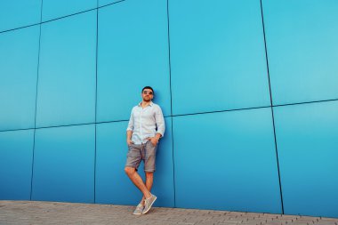 Karanlık güneş gözlüğü kentsel bir adamla kavramı. Çekici. Serin adam. Şort giyiyor. Mavi duvarın önünde duran.