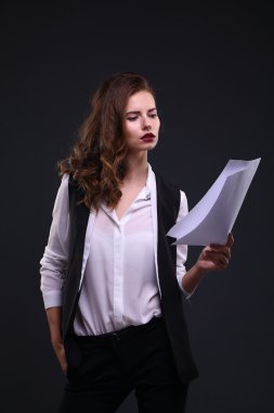 Beautiful business lady holding white sheet of paper on a dark background. Studio shot