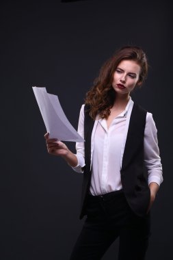 Beautiful business lady holding white sheet of paper on a dark background. Studio shot