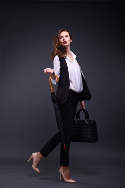 İş kadını bir siyah ceket Beyaz tişört, şemsiye, karanlık bir arka plan üzerinde el çantası. Stüdyo vurdu.