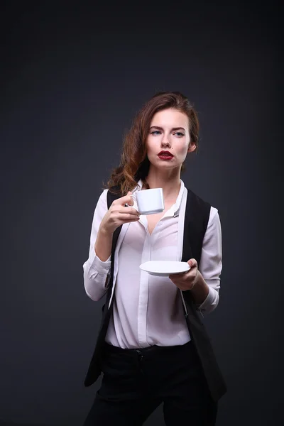 Hermosa dama de negocios sosteniendo una taza de café blanco sobre un fondo oscuro. Captura de estudio —  Fotos de Stock