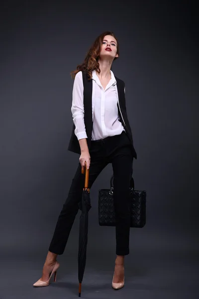 Красивая деловая женщина в чёрной куртке, белой рубашке, зонтике, сумочке на тёмном фоне. Снимок студии . — стоковое фото