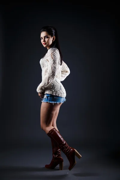 Όμορφη μελαχρινή κοπέλα σε μπεζ πουλόβερ, μπλε σορτς, χτένισμα — Φωτογραφία Αρχείου