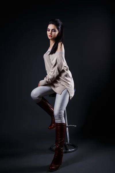 Piękna brunetka dziewczynka w beżowy sweter, dżinsy, fajne fryzury, siedząc na pasku stołek — Zdjęcie stockowe