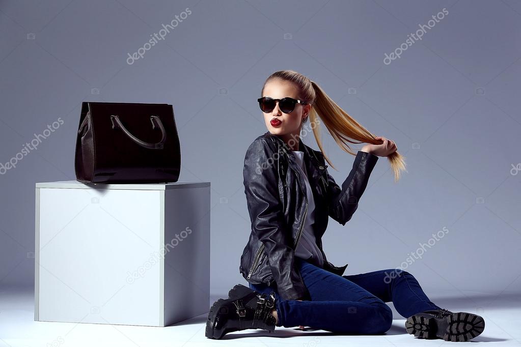 portrait of Vogue style beautiful young blond woman with black bag near cube in studio