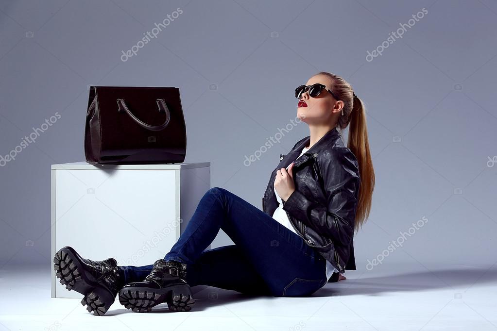 portrait of Vogue style beautiful young blond woman with black bag near cube in studio
