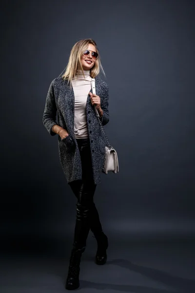 Menina Beleza Sexy. Loira de moda. Retrato de uma menina vestida de casaco cinza e óculos de sol, vestindo um saco bege posando em um fundo cinza . — Fotografia de Stock