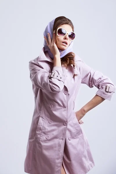 Молода мода жінка позує в студії в рожевому пальто і білих сонцезахисних окулярах . — стокове фото