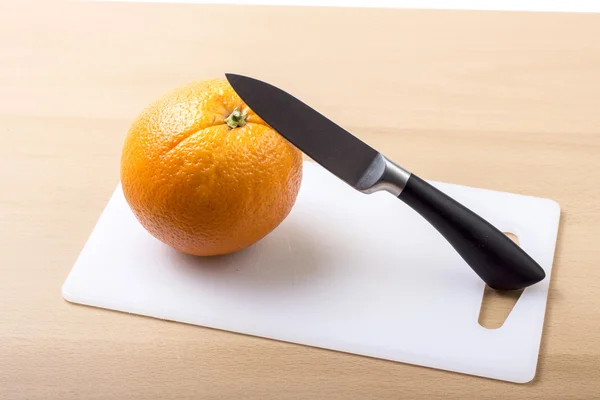 Orange on white cutting board with knife — Stock Photo, Image