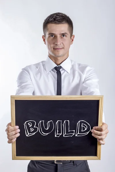 BUILD - Young businessman holding chalkboard with text — Stock Photo, Image