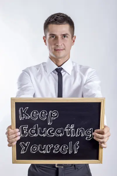 Hålla utbilda dig (nyckel) - ung affärsman holding svarta tavlan med text — Stockfoto