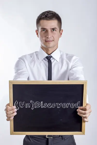 (un) entdeckt - junger Geschäftsmann hält Kreidetafel mit Text — Stockfoto