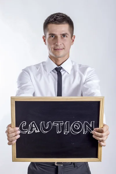 CAUTION - Young businessman holding chalkboard with text — Stock Photo, Image