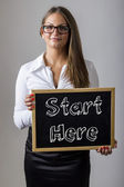 Start hier - junge Geschäftsfrau hält Tafel mit Text in der Hand
