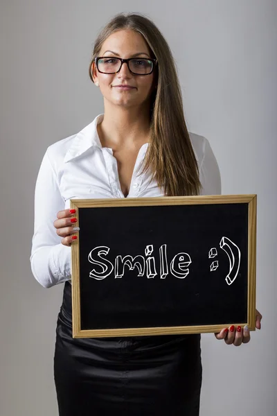 Smile :) - Young businesswoman holding chalkboard with text — Stockfoto