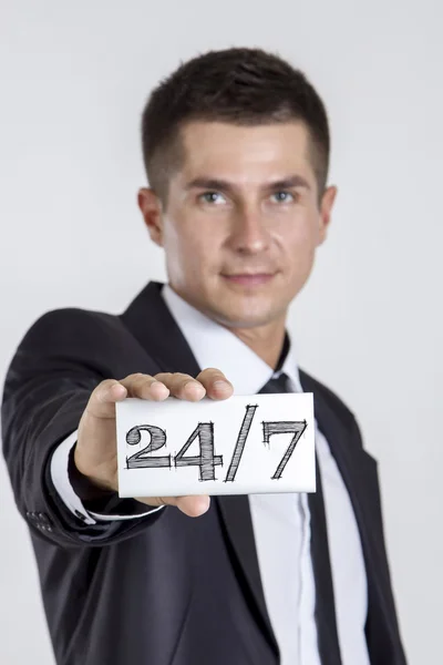 24/7 - mladý podnikatel drží bílou kartu s textem — Stock fotografie