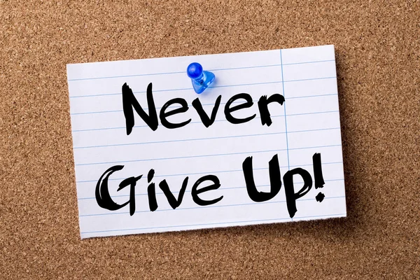 Never Give Up! -gescheurd nota papier vastgemaakt op prikbord — Stockfoto