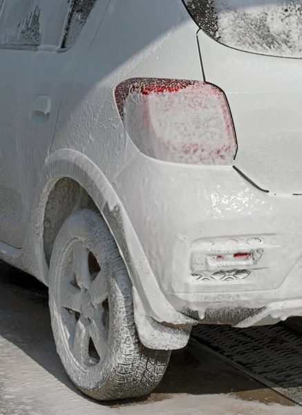 white car in soap foam on the car wash
