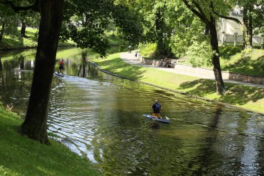 Riga şehir parkındaki kanalda, erkekler yemeklerle yüzer.