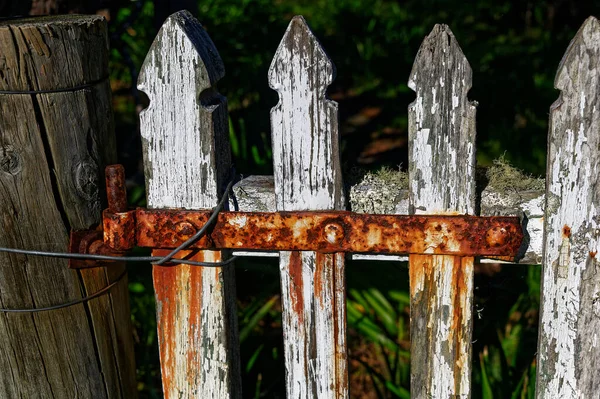 A white picket fence with a rusty red hinge