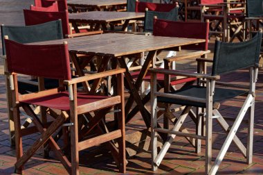 Dışarıda bir kafe, branda, ahşap masalar ve sandalyeler var..