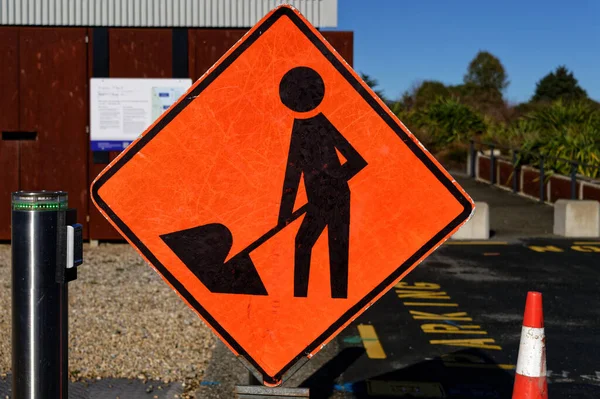 An orange diamond sign with a figure of a person at work warns of potential danger