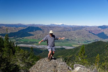 Bir adam, arkasında dağ ve vadi olan kayalık bir çıkıntının tepesinde dans etmekten zevk alır.
