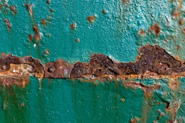 Rust is eating away at the teal paint on a metal door