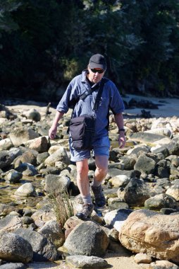 Yaşlı bir adam kıyıdaki kayaların üzerinden atlıyor.