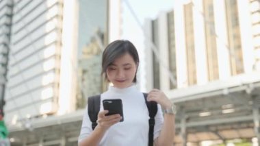 Mutlu Asyalı kadın caddede yürüyor ve akıllı telefon kullanıyor. Pozitif duygu