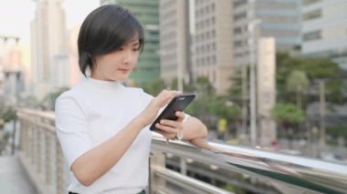 Mutlu Asyalı kadın caddede yürüyor ve akıllı telefon kullanıyor. Pozitif duygu