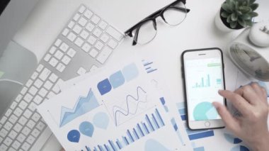 İş kadınının elleri çalışıyor ve grafik veri belgesi ile akıllı telefon kullanıyor