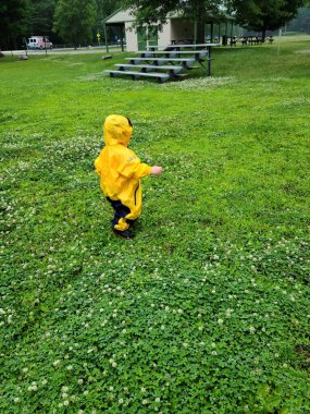 Küçük çocuk yağmurluk giymiş çimenlerde yürüyor.
