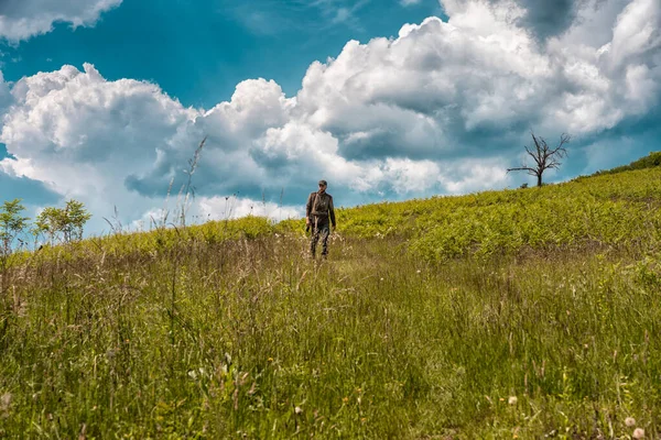 Young hunter climbing a hill in search for prey with beautiful cloudscape behind him