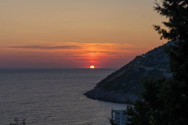 Kızıl Güneş ufukta batıyor. Önünde dağlar var.