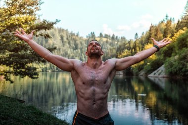 Arka planda muhteşem bir Spajici gölüyle güneş ışığını kucaklayan kaslı genç adam.