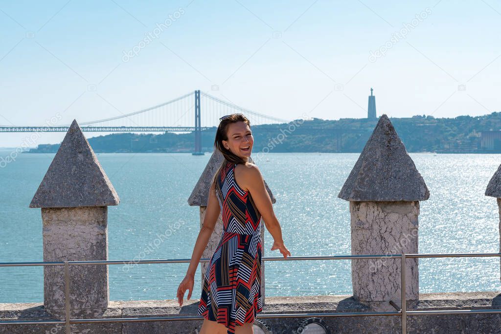 Young beautiful woman smiling on Belem tower with Tagus river and Ponte 25 de abril in the background