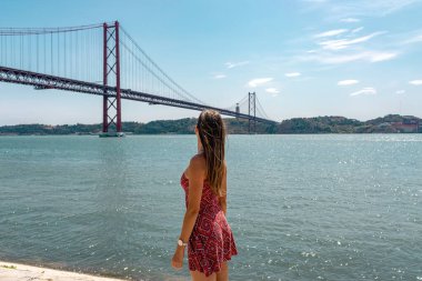 25 Nisan ve Tagus Köprüsü ya da Keşifler Anıtı 'ndan Tejo Nehri. Padrao dos Descobrimentos platformunda kollarını açmış mutlu turist kadın. Belem Bölgesi, Lizbon, Portekiz. Avrupa seyahat kavramı.